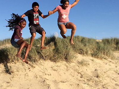 Gabbi, Julian and Samara jumping from a sand dune.